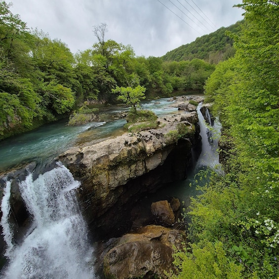 A waterfall cascading over a rocky ledge surrounded by lush greenery. 5