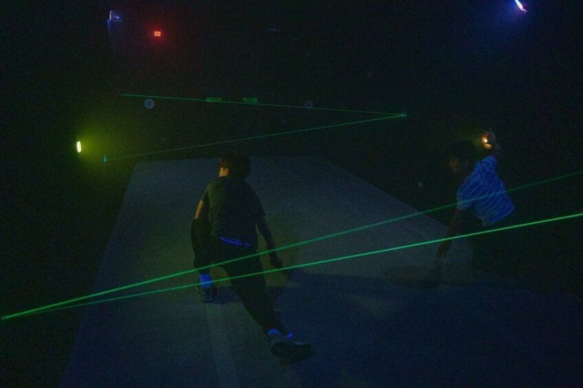 Two people in a dark room with green laser lines on the floor. 2