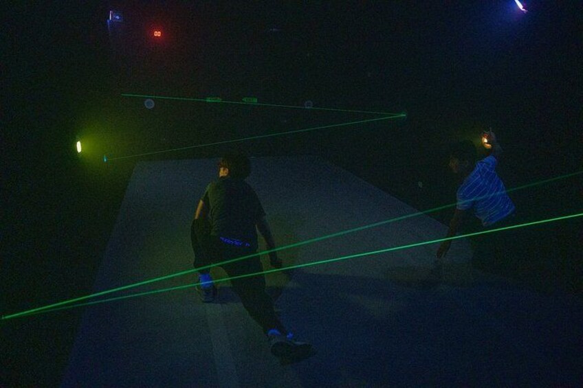 Two people in a dark room with green laser lines on the floor. 3