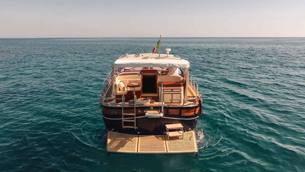 A boat with a covered deck, a flag, and a wake in the water. 2
