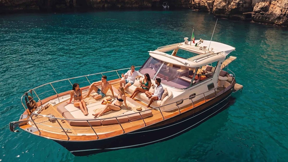 A boat with people relaxing on deck, surrounded by clear turquoise water and rocky cliffs. 1