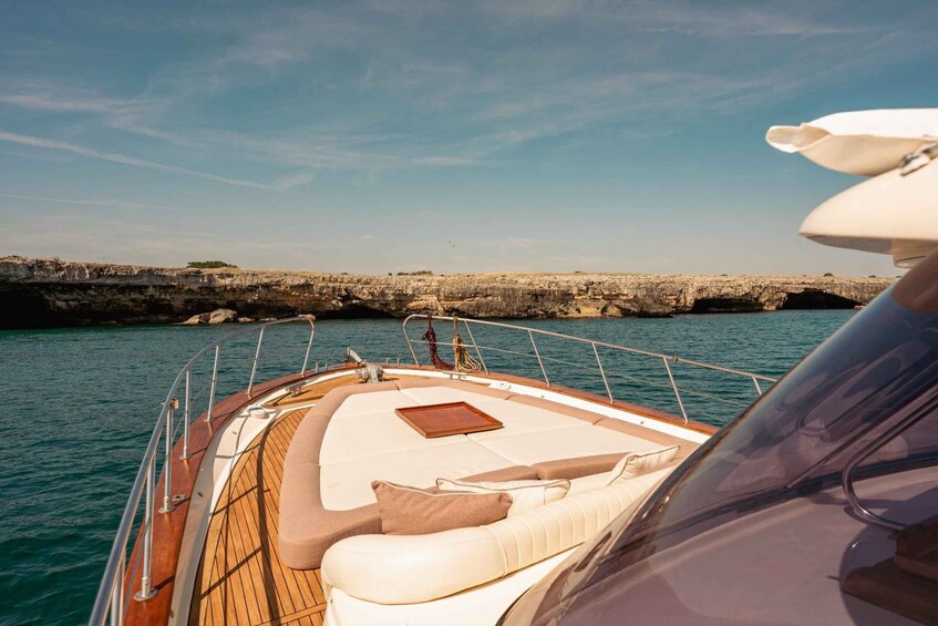 A boat with a wooden deck, white cushions, and a view of rocky coastline. 3