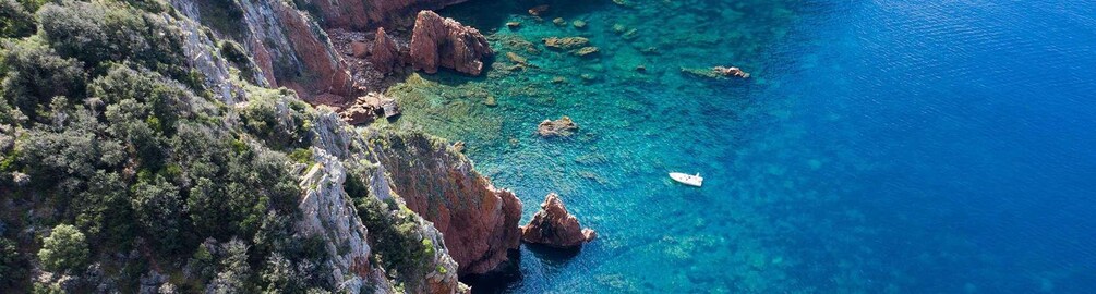 A coastal landscape with rocky cliffs, clear blue water, and a small boat. 1