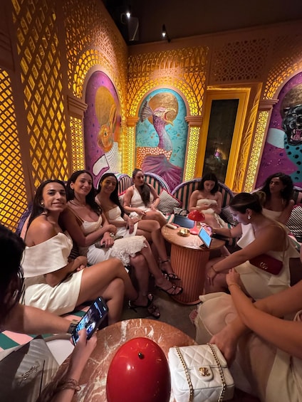 A group of people seated in a room with ornate wall decorations and a large mural. 3