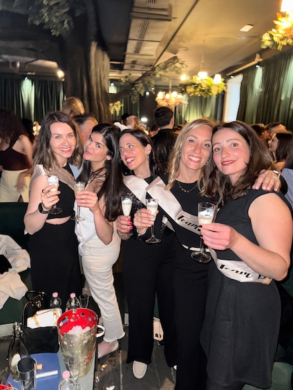 A group of people at a social event, holding drinks and wearing sashes. 1