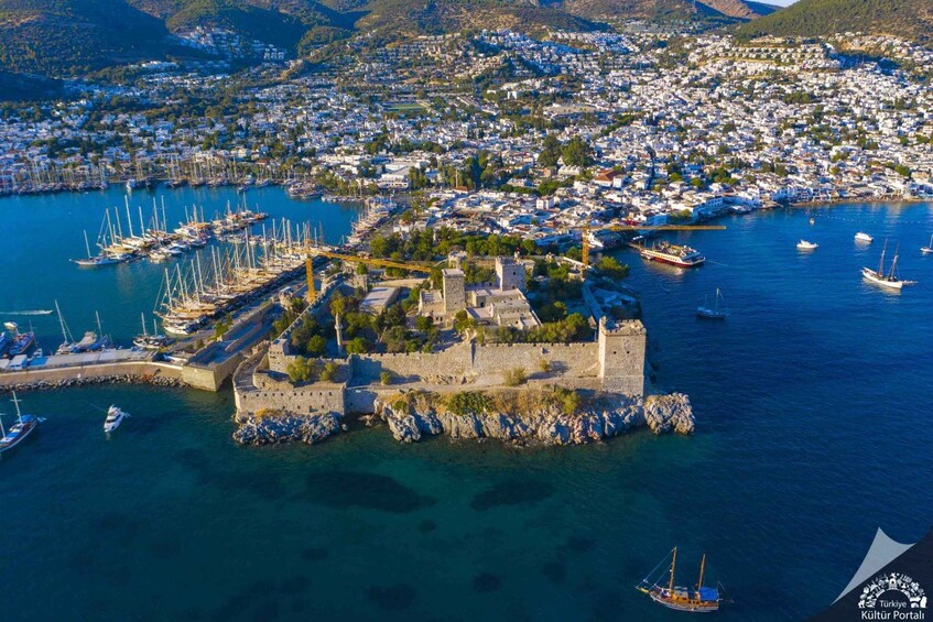 A coastal town with a historic castle surrounded by a harbor filled with boats. 1