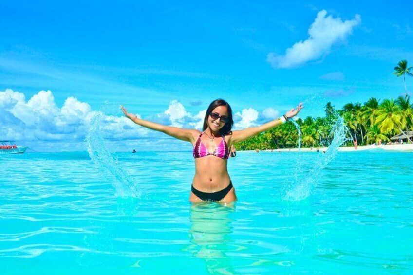 A person in a bikini in clear blue water with a boat and palm trees in the background. 4