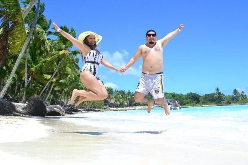 Two people jumping on a beach with palm trees and clear blue water in the background. 1