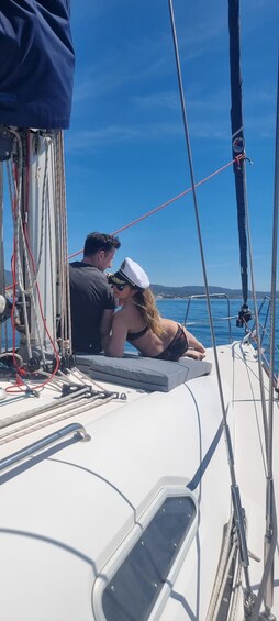 A sailboat with two people on deck, a clear blue sky, and calm waters. 2