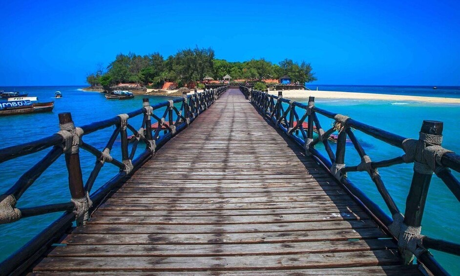 A wooden pier leading to a beach with clear turquoise waters and a small island in the distance. 3