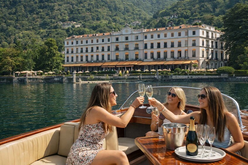 A boat with three people toasting with champagne glasses, a large building in the background, and a body of water. 1