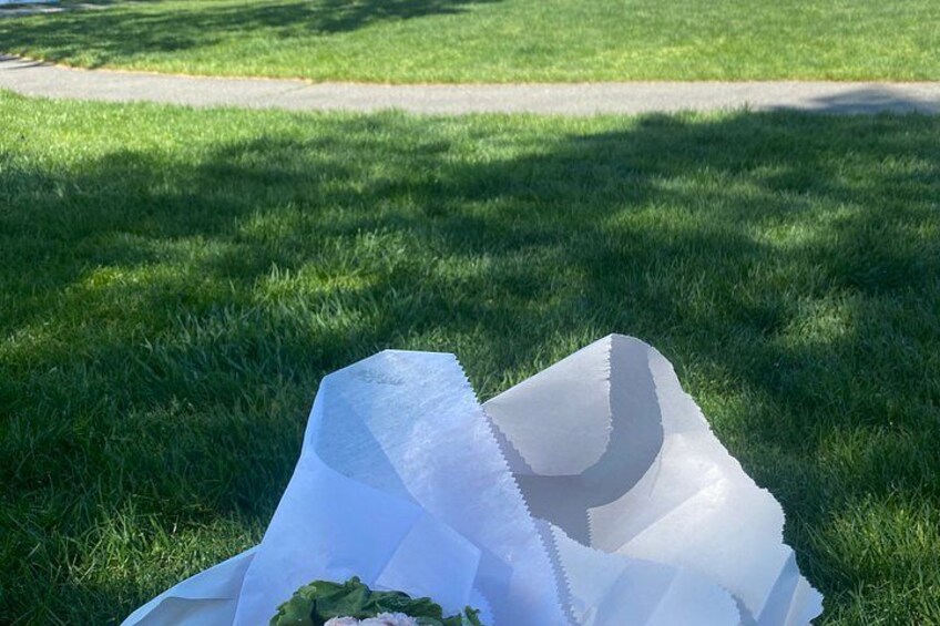 A white paper bag on grass with a bouquet of flowers. 1