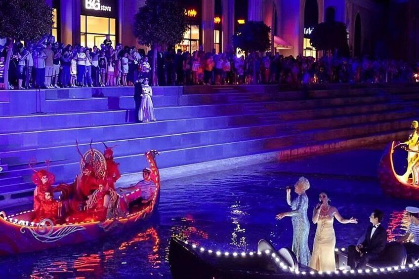 Una función nocturna al aire libre con artistas en barcos y escalones, iluminada por luces de escenario. 5