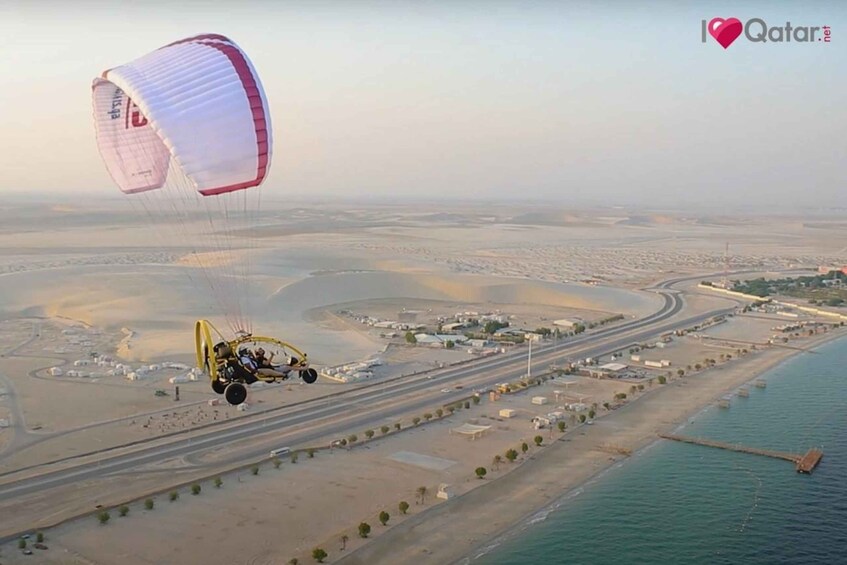 A paraglider flying over a coastal area with roads and buildings. 4