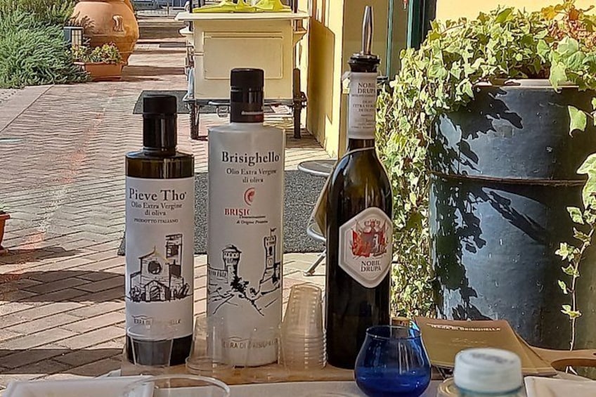 Three bottles of olive oil, a blue glass, and a metal container on a table. 3