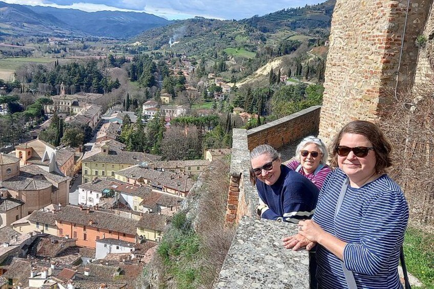 Un gruppo di persone in piedi su un muro di pietra, con vista su una città, edifici e colline sullo sfondo. 3