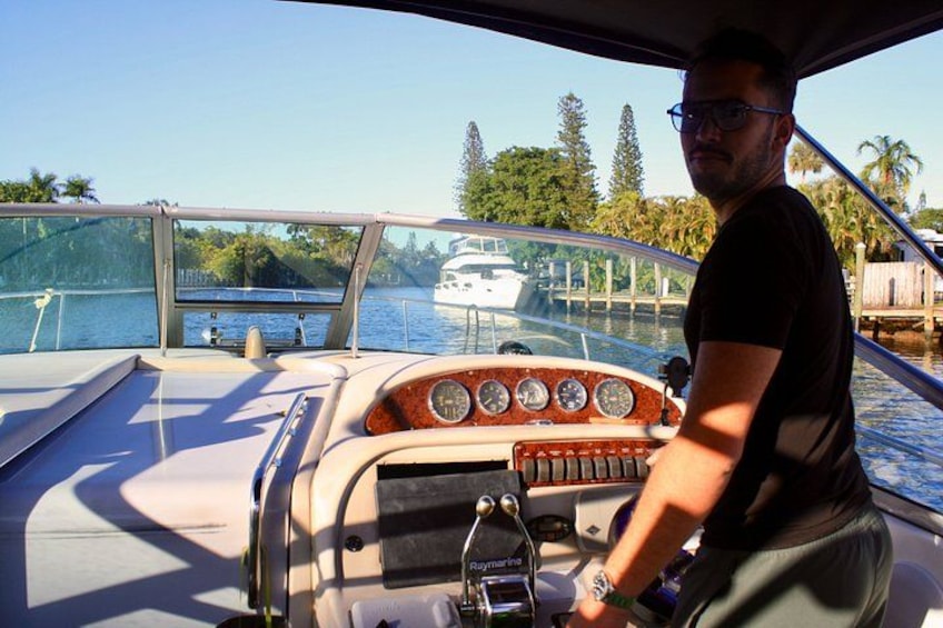 Una persona manejando un bote en una vía fluvial tranquila, con cielo despejado y vegetación al fondo. 3