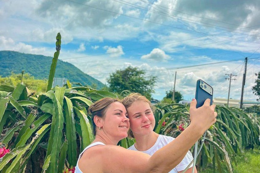 Twee personen maken een selfie met een smartphone, omringd door groene begroeiing en een bergachtig landschap. 4