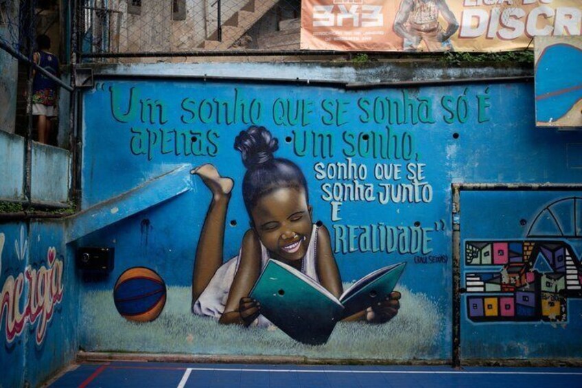 A mural with a child reading a book, a basketball, and a quote in Portuguese. 2