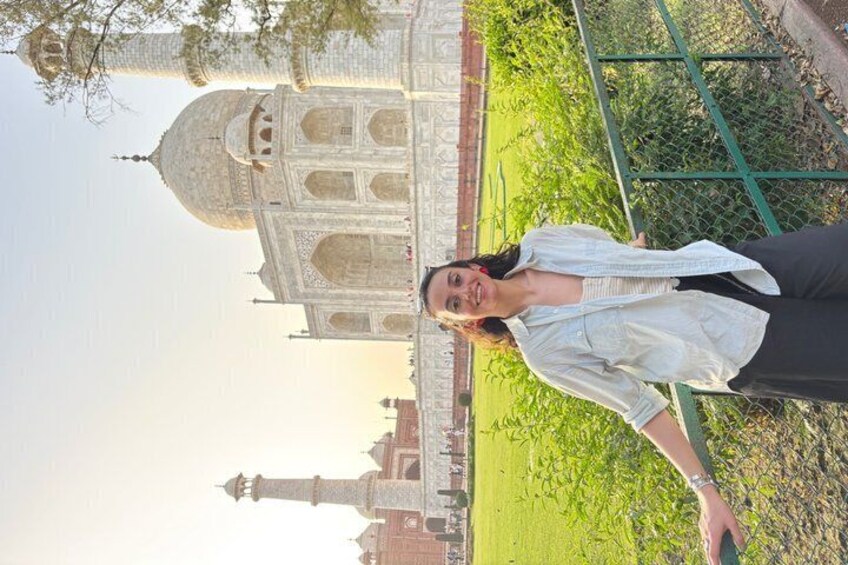 A person standing in front of the Taj Mahal with a green fence and a garden in the background. 5