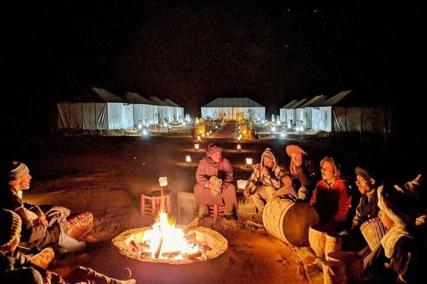 A group of people gathered around a campfire at night, with tents in the background. 2