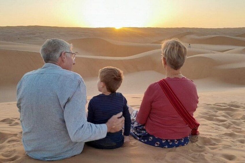 Three people sitting on sand dunes facing a sunset. 1