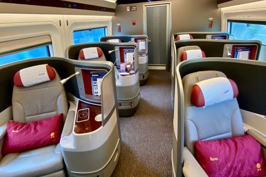 A train carriage with reclining seats, personal entertainment screens, and a window. 5
