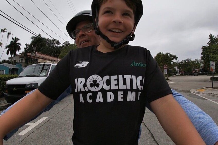Eine Person mit schwarzem T-Shirt, auf dem 'JROCK CLEVELT ACADEMY' steht, steht auf einer Straße. Im Hintergrund sind ein weißer Van und Palmen zu sehen. 5