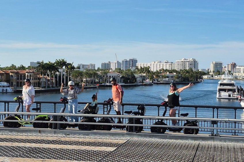 A waterfront with people standing on a dock, a boat in the water, and buildings in the background. 4