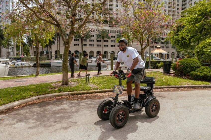 A person riding a Segway on a paved path in a park with trees and a body of water in the background. 5