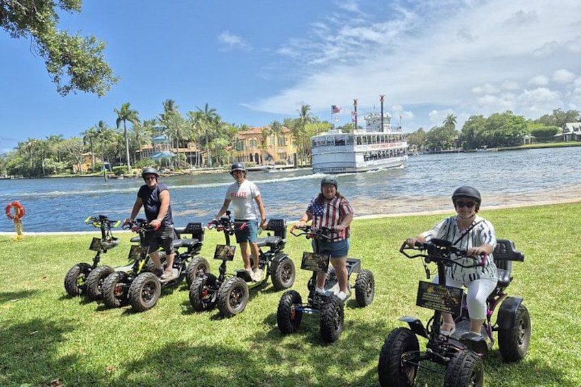 Four people on Segways near a waterfront with a boat and palm trees in the background. 5