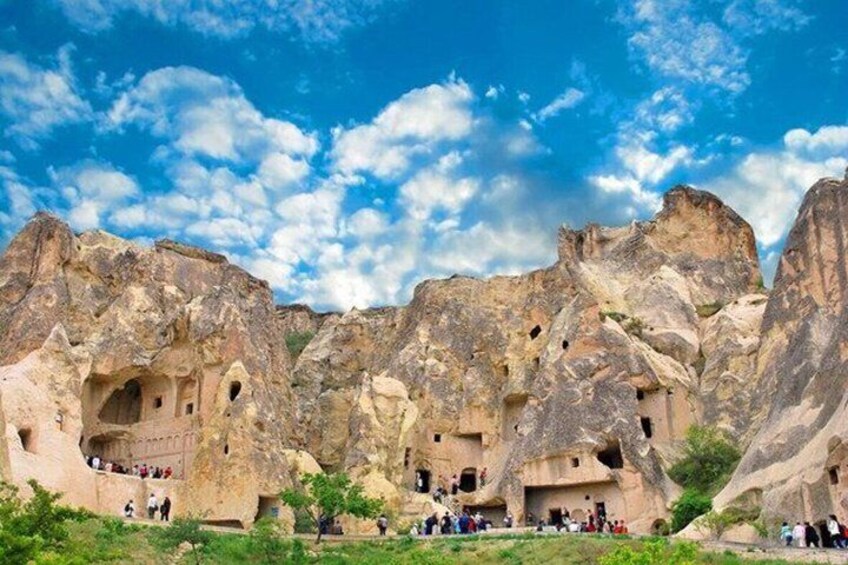 A rocky landscape with cave dwellings and visitors. 3