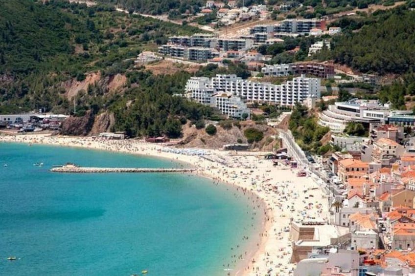 A coastal town with a beach, buildings, and a forested hillside. 5