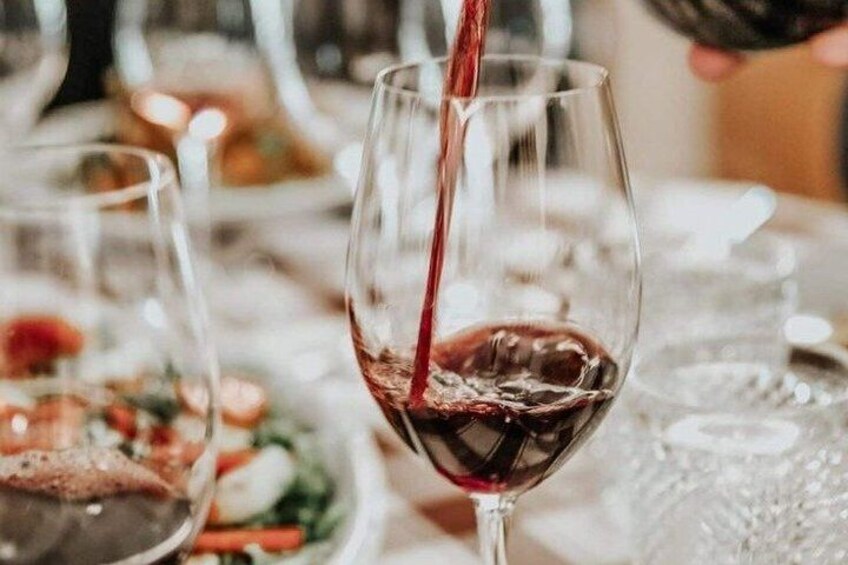 A glass being filled with red liquid, likely wine, in a dining setting. 2
