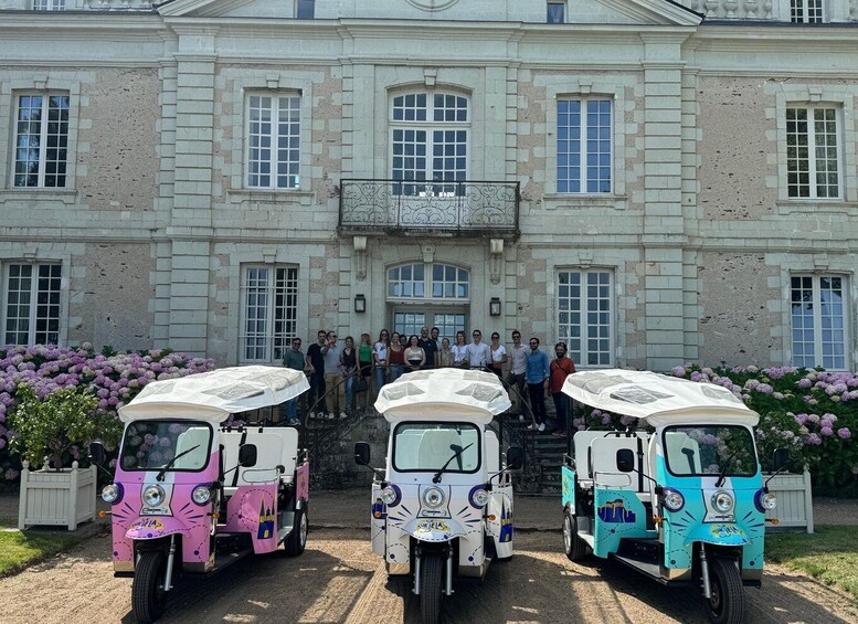 A group of people standing in front of a large building with three tuk-tuks parked in front. 3