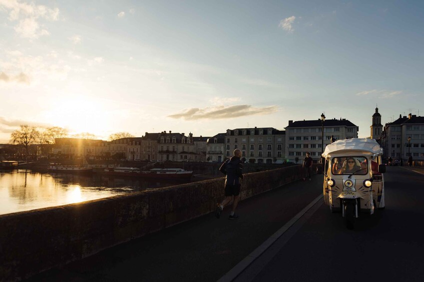 A sunset over a river with buildings and a tuk-tuk on a bridge. 1
