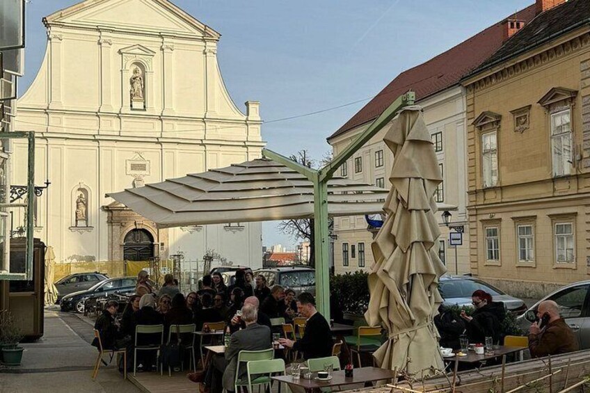 Eine Gruppe von Personen speist draußen in einem Café unter einer weißen Markise. 5