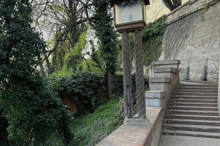 Eine steile Steintreppe führt einen Hügel hinauf, umgeben von Grün und einem Gebäude im Hintergrund. 2