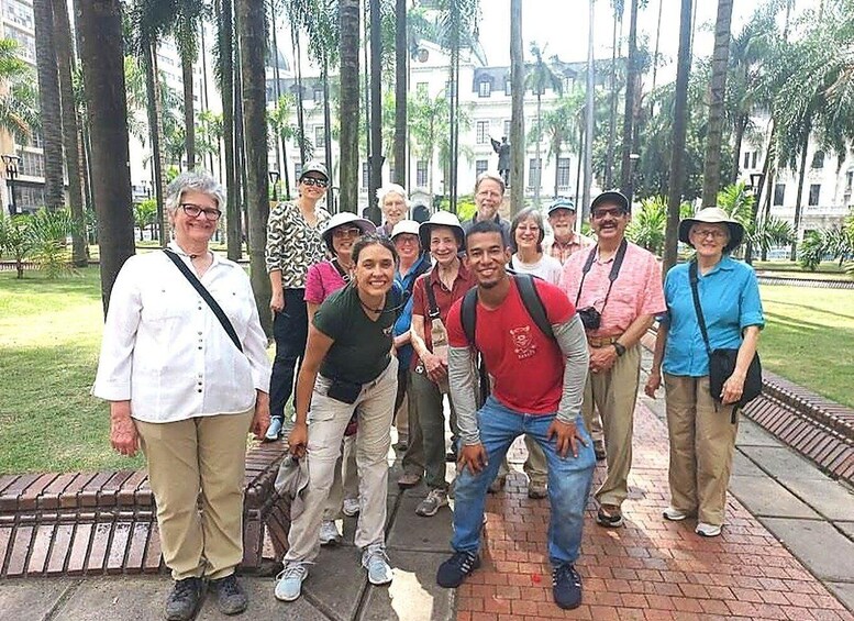 A group of people standing outdoors in a park with trees and a building in the background. 2