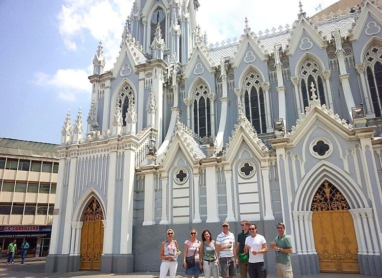 A group of people standing in front of a grand, ornate building with Gothic architecture, featuring pointed arches and intricate detailing. 1