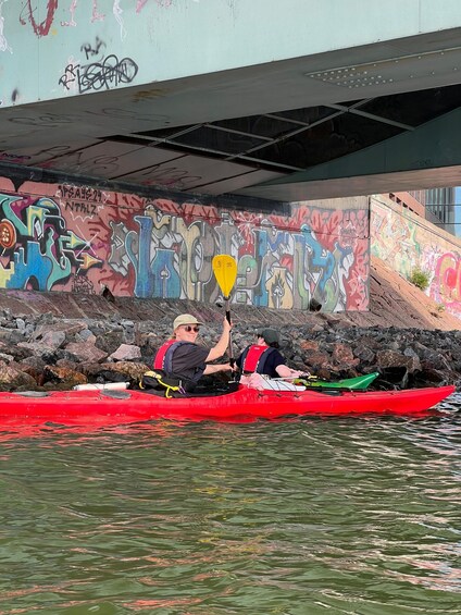 Two people kayaking under a bridge with graffiti-covered walls. 2