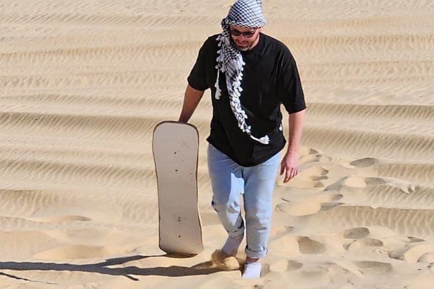 En person som går på sanddyner med ett snowboard. 4