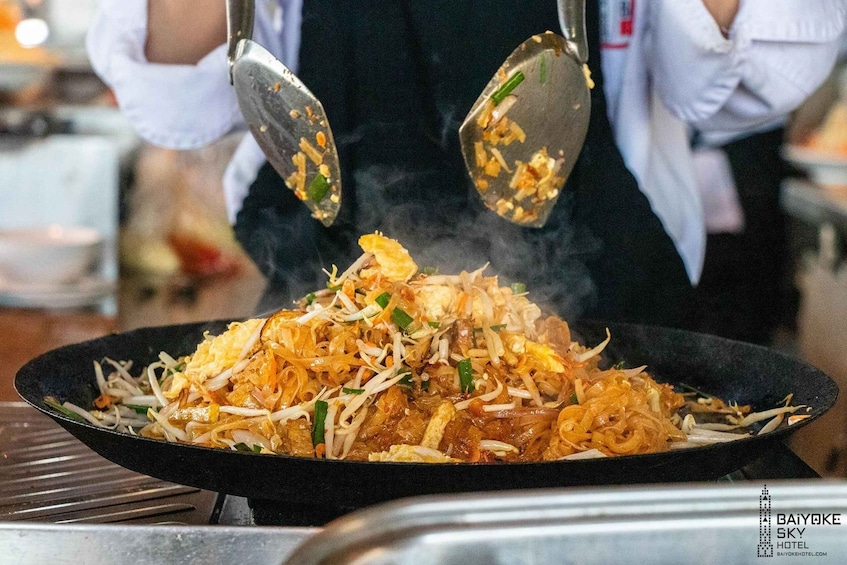 A person cooking stir-fried noodles with vegetables and scrambled eggs in a wok. 5