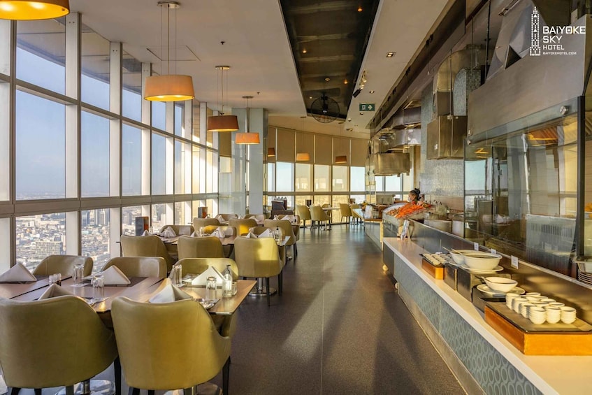 A modern restaurant with high ceilings, large windows, and a buffet counter. 1