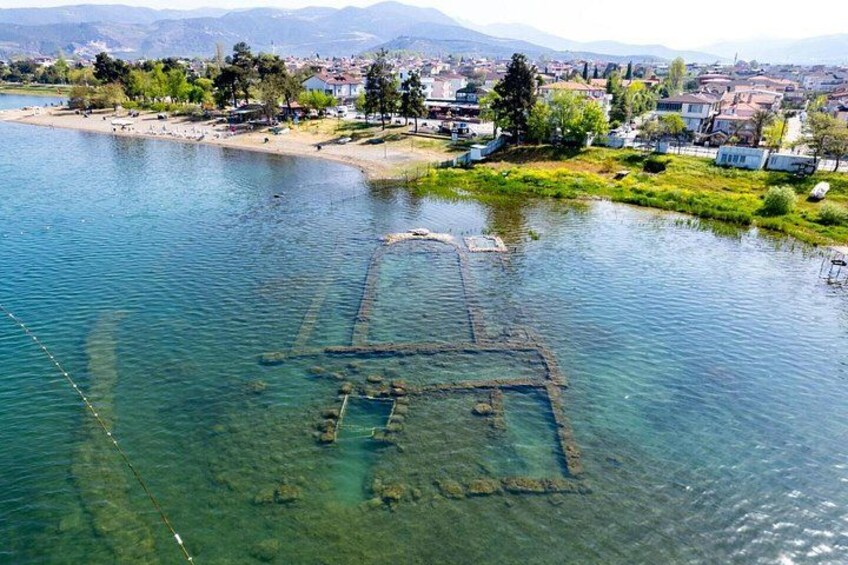 En klar sjö med en nedsänkt konstruktion, en strand och en stad i bakgrunden. 2