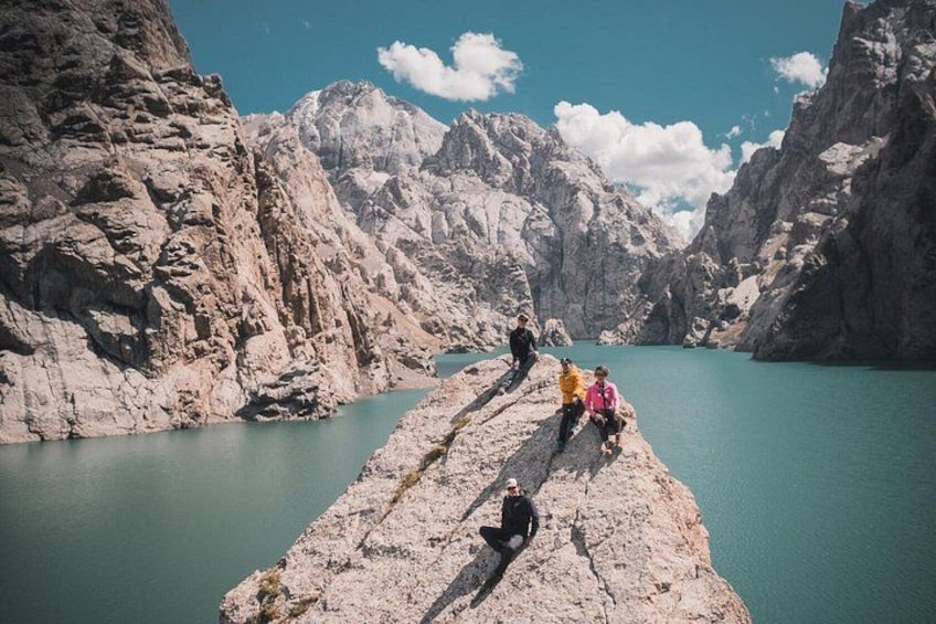 Eine Gruppe von Personen auf einer Felsstufe mit Blick auf einen türkisblauen See, der von schroffen Bergen umgeben ist. 1