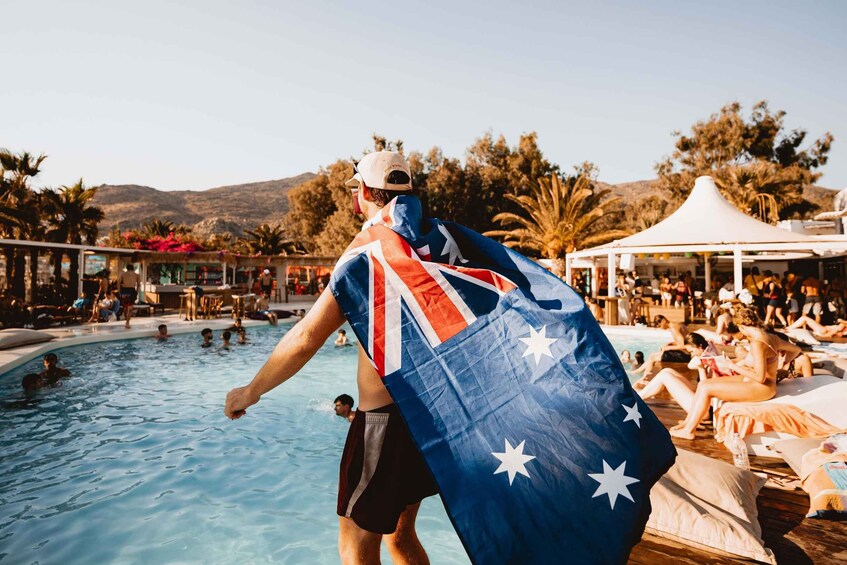 A person holding an Australian flag by a poolside with people lounging and a tent in the background. 3