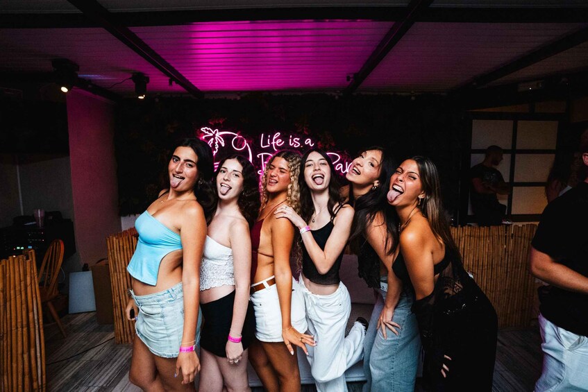 A group of people in a dimly lit room with a neon sign that reads 'Life is a Party.' 5