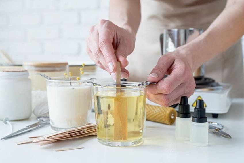 Hands stirring a liquid in a glass container, surrounded by jars and bottles on a white surface. 5
