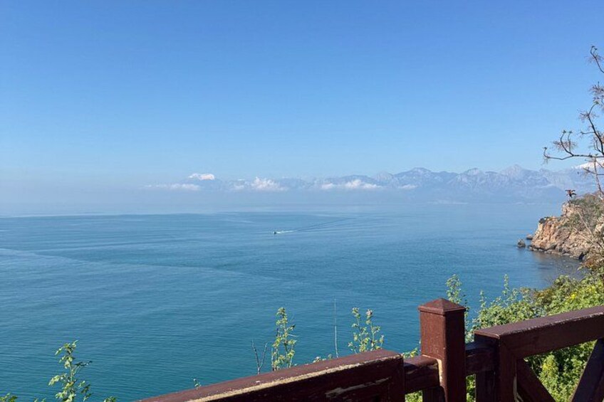 A coastal view with a wooden railing, calm sea, and distant mountains. 5
